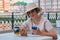 A woman in a straw hat with a smartphone sits in a street cafe and eats her dessert