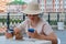 A woman in a straw hat with a smartphone sits in a street cafe and eats her dessert