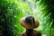 woman with straw hat standing in tropical forest jungle on rainy day. rain season. rear view