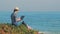 Woman in straw hat using laptop on holidays, beautiful coastline