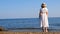 woman in a straw hat and white dress walks along the seashore and admires the blue sea on a sunny summer day, enjoying