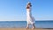 woman in a straw hat and white dress walks along the seashore and admires the blue sea on a sunny summer day, enjoying