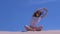 Woman stretch sits lotus pose sandy beach hands up tilts in side windy day sky.