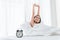 Woman stretching and happy smile on bed in bedroom. Wake up by alarm clock in morning