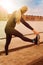 Woman stretching legs exercise training fitness outside by the boardwalk in yellow sun raysat an urban harbor.