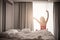 Woman stretching near bed after waking up with sunrise at morning, back view