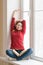 Woman stretching sitting on a windowsill with a book