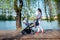 Woman with stroller on lake deck on city park. Happy mother walking child with pram