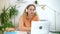 Woman student talking and using laptop, sitting at the table in home interior.