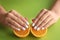 Woman with stylish nails holding halves of orange on color background, closeup