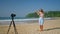 Woman in stylish sportswear performs dance recorded on camera at tropical beach. Solo female influencer creates content