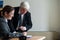 A woman in a suit signs documents under the direction of a mature male boss. Friendly colleagues talking in the office