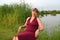 The woman in a summer claret dress sits on the bank of the lake