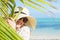 Woman with summer hat on the beach hiding behind palm leaf