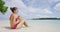 Woman sunbathing sitting on beach in bikini drinking from coconut