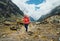 Woman in sunglasses with backpack and trekking poles dressed red softshell jacket hiking during Makalu Barun National Park trek in