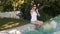 Woman in sunglasses and casual wear sits on edge of pool, holds feet in water