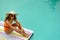 Woman in sunglasses and hat sitting at the edge of swimming pool