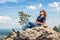 Woman with sunglasses relaxing on mountain peak in summer. Landscape and happy beautiful person sunbathing on cliff. Adult pretty