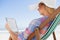 Woman in sunhat sitting on beach in deck chair using tablet pc