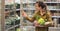 Woman in the supermarket. Beautiful young woman holds in hands fresh organic vegetables and opens the fridge in the supermarket