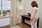 A woman sweeps dust with a brush from a piano in a home living room, cleaning musical instruments