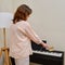 A woman sweeps dust with a brush from a piano in a home living room, cleaning musical instruments