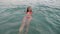 Woman swims in the sea, falls into the water and have fun, looking at camera