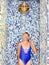 Woman in swimsuit standing under pouring ice water bucket in wellness area