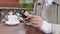 Woman swipes in the phone sitting at a table with a cup of coffee on the terrace. Close-up view of hands with cell phone