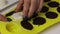 A woman takes out chocolate glazed candies from a silicone form