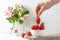 Woman takes or puts one strowberry in fruit bowl full of fresh, red, jucy strawberries. Pastel-colored decoration.