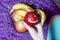 A woman takes a red apple with a carved emoticon from a dish. There is a fruit basket in the background. Several apples and banana