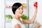 Woman takes red pepper from opened fridge