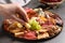 Woman taking cheese from plate with different appetizers on grey table, closeup