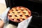 Woman taking freshly baked cherry pie out of oven, closeup