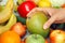 A woman taking a mango out of a pile of fruit and vegetables