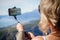 Woman taking panoramic picture of mountain landscape. Selfie photo stick