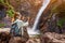 Woman taking photo of majestic waterfall in the jungle. Hiking and sightseeing concept