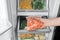 Woman taking plastic bag with frozen carrot from refrigerator