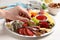 Woman taking sausage from plate with different appetizers on white wooden table, closeup