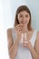 Woman taking vitamin pill with glass of fresh water indoors