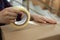 Woman taping cardboard box indoors, closeup view