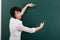 Woman teacher shows on a blackboard anything, blank space for text and graphics, green background, Studio shot