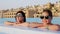 Woman and teen girl, mom and daughter, in funny, identical, round sunglasses, relax in water of outdoor pool with