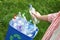 Woman throwing used bottle into trash bin outdoors. Plastic recycling