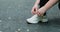 Woman ties her shoelaces on her sneakers. Process of lacing sneakers on asphalt background.