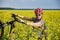 Woman tilts her mountain bike while looking at the camera. Portrait in nature, in a rapeseed field