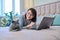 Woman together with cat lying on bed at home, female using laptop