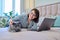 Woman together with cat lying on bed at home, female using laptop